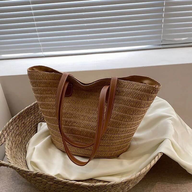 Bolsa trançada de palha caqui com alça de couro da Loja Morela, ideal para looks de verão e estilo casual.