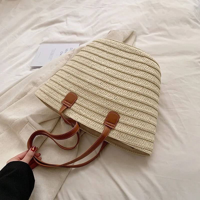 Bolsa trançada de palha bege com alça de couro da Loja Morela, ideal para looks de verão e estilo casual.