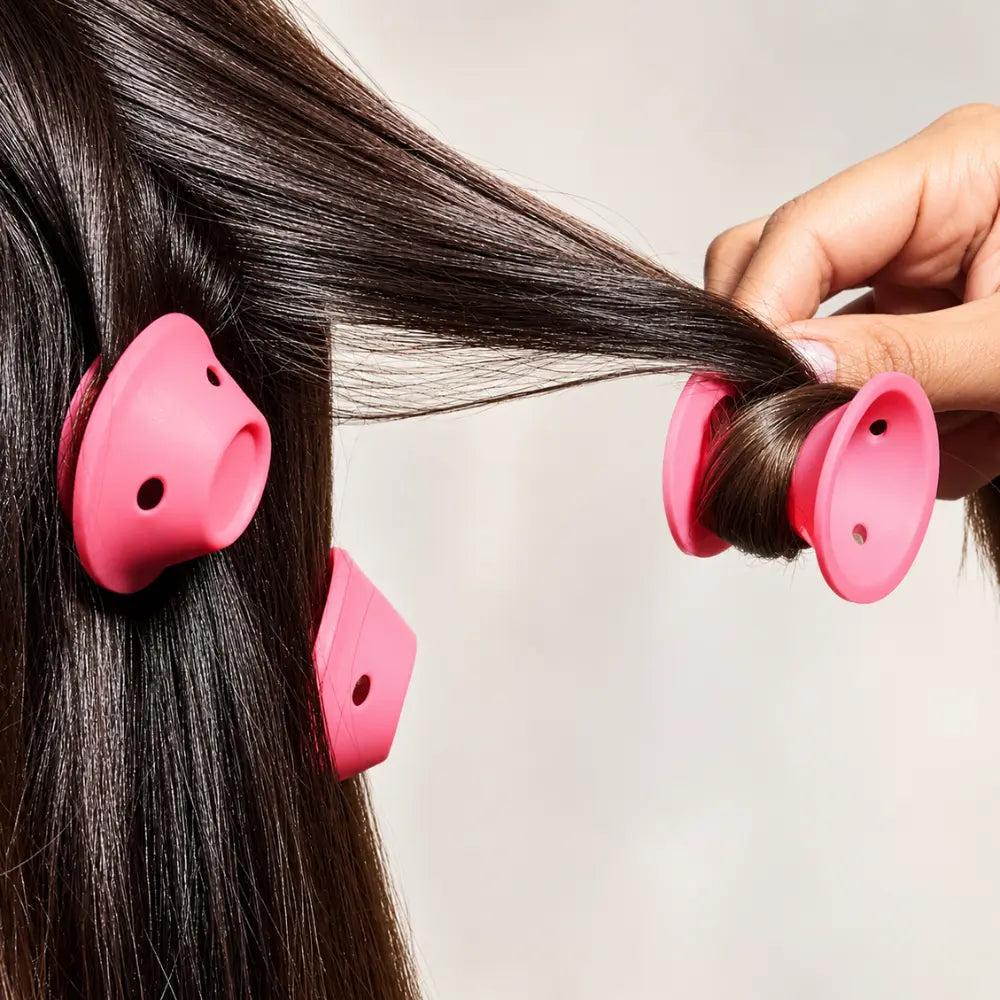 Mão enrolando uma mecha de cabelo castanho em um modelador de silicone rosa.