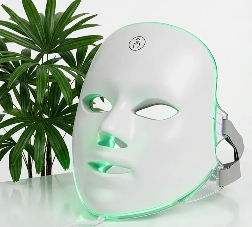 Máscara de LED facial branca posicionada sobre uma mesa de skincare com luz verde ativada Loja Morela
