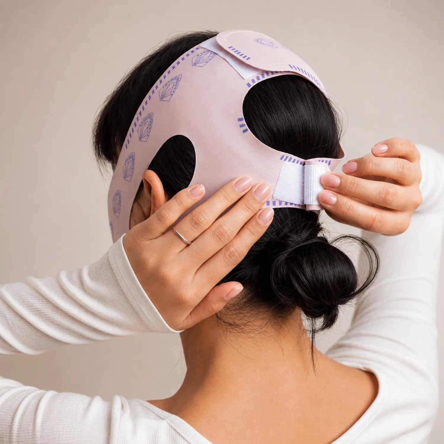 Visão posterior de mulher ajustando o fecho aderente na parte de trás da cabeça e nuca da máscara modeladora facial V-Line Loja Morela